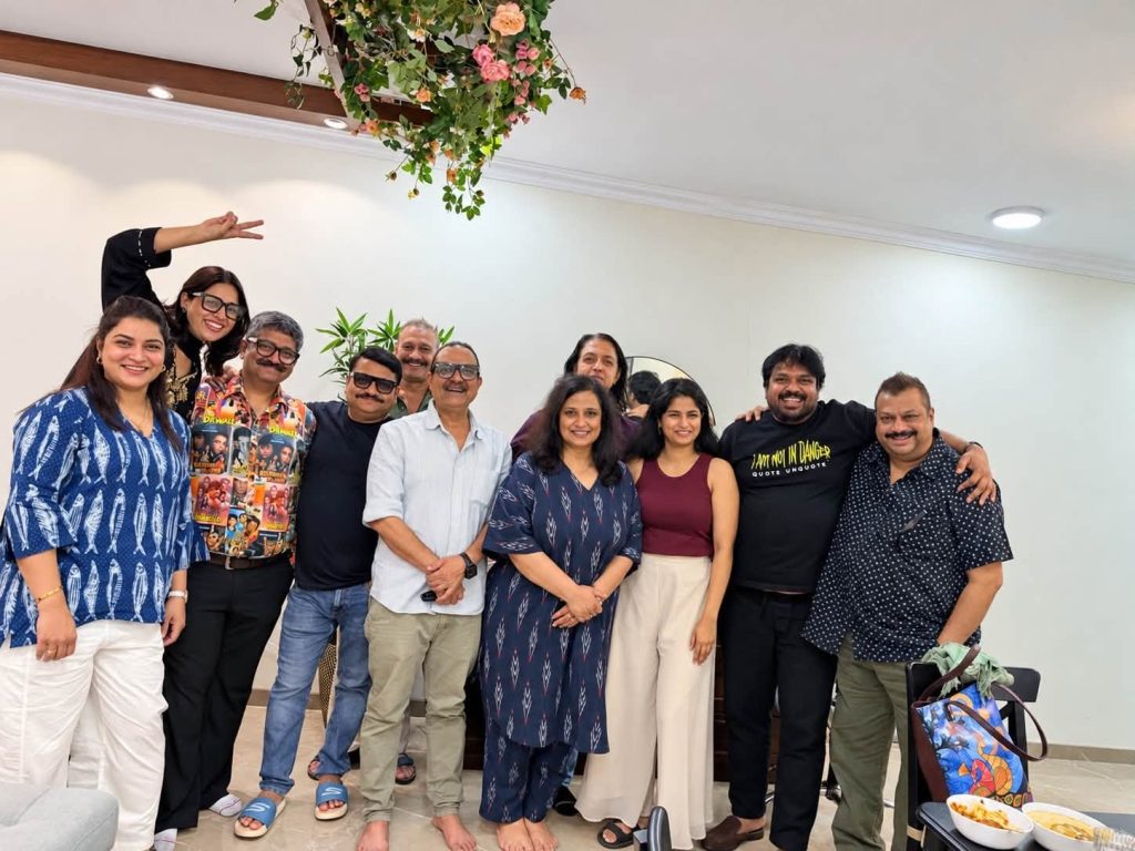 sanjay sharma_1 | No. 1 Indian Media News Portal Group of smiling colleagues posing together in a bright room with plants and hanging flowers above them, casual attire.