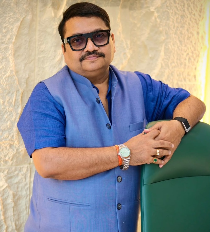 sanjay sharma_2 | No. 1 Indian Media News Portal Man in a blue traditional jacket leaning on a green chair, wearing sunglasses and a watch.