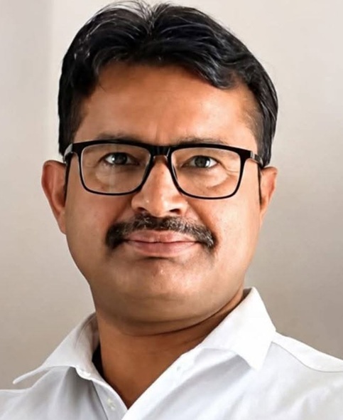 shashi shekhar nkb | No. 1 Indian Media News Portal Close-up portrait of a man with dark hair and black rectangular glasses, wearing a white collared shirt and a neutral expression.