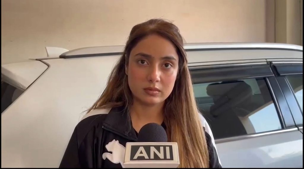 Female reporter holding a microphone with ANI logo, standing beside a white SUV.