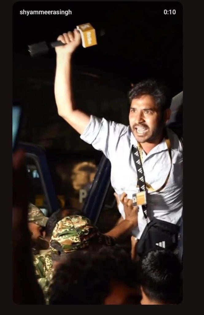 shyam | No. 1 Indian Media News Portal Man on a raised platform shouting, raising a yellow-microphone in his right hand as a dense crowd reaches up toward him at night.
