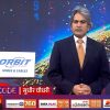 Male news anchor in a dark suit and orange tie stands in a TV studio, with an Orbit Wires & Cables sign on a lectern to his left and a colorful digital backdrop behind him.
