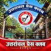 Gate to Uttarakhand Press Club featuring a blue arch sign, a red circular emblem of a hand holding a pen, and bold Hindi text.